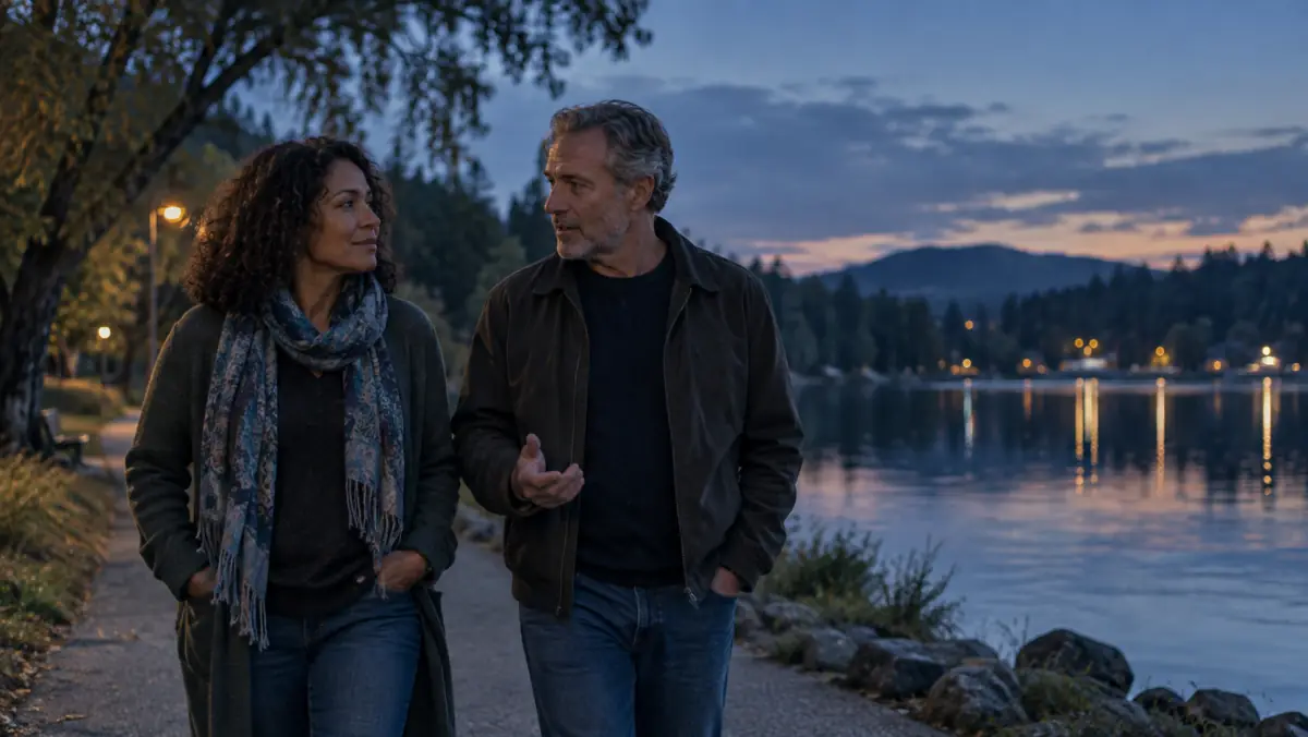 An adult couple talking while walking beside a quiet lake at dusk.